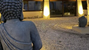 Uma estátua de Buda em um jardim, com um edifício ao fundo.