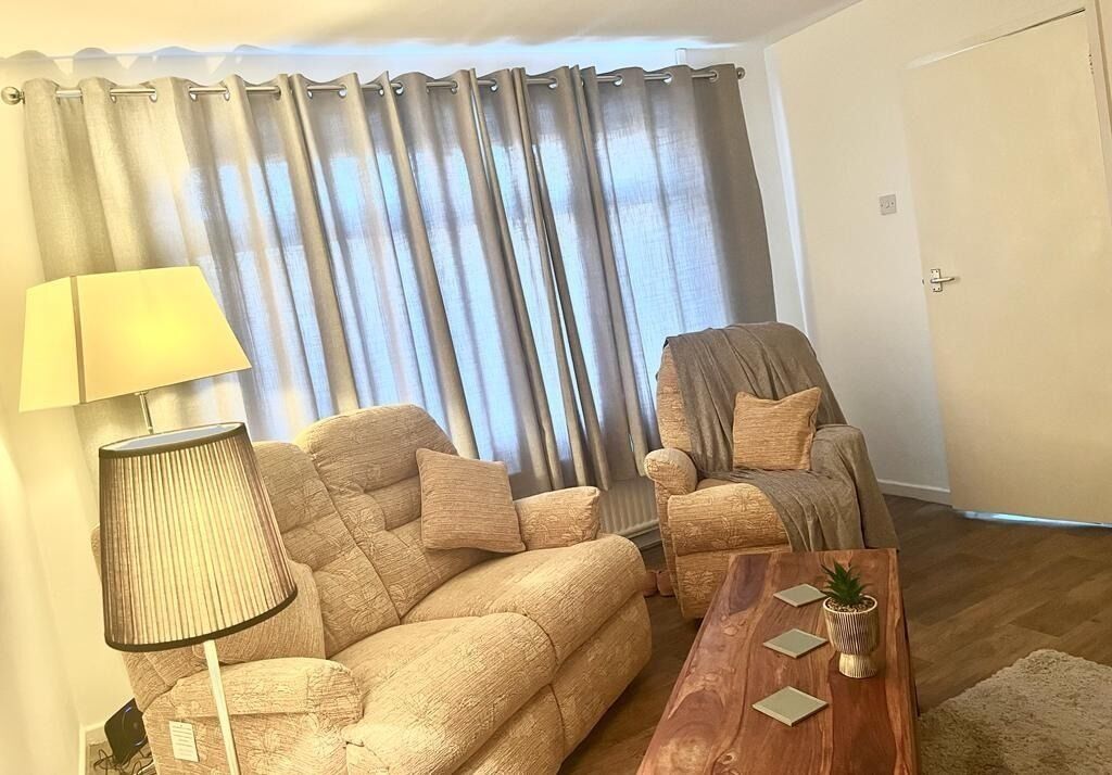 A living room with a sofa, armchair, lamp, coffee table, and curtains.