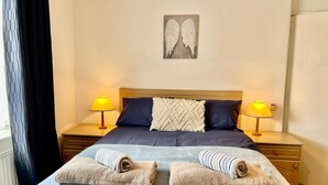 A neatly made bed with two towels, a wall art of wings, and two bedside lamps. - Spacious Family Home (Manchester)