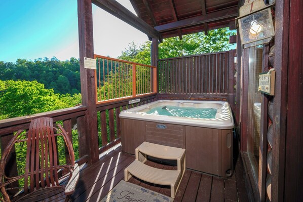 A wooden deck with a hot tub, a wooden chair, and a small step stool.
