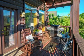 A wooden deck with outdoor furniture, a grill, and a view of greenery.