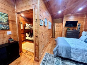 A wooden cabin bedroom with a bunk bed, a flat-screen TV, a dresser, and a rug.