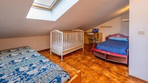 A room with a sloped ceiling, a crib, a bed, and a desk.