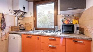 A compact kitchen with a window, a microwave, and orange cabinets.