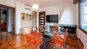 A modern kitchen with a dining area, featuring a glass table, metal chairs, a built-in TV, and a fireplace.