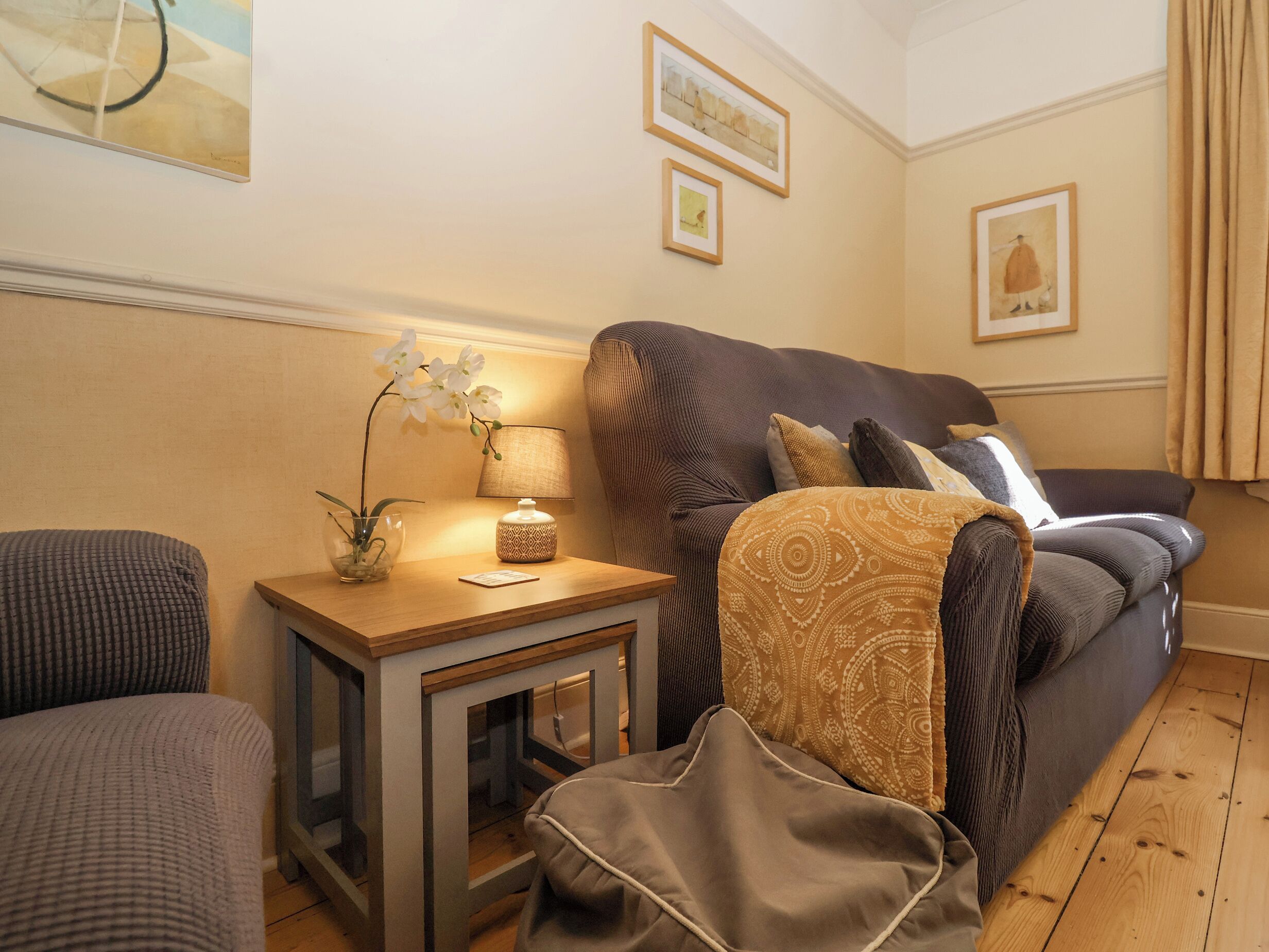 A cozy living room with a sofa, a side table with a lamp, and a small plant.