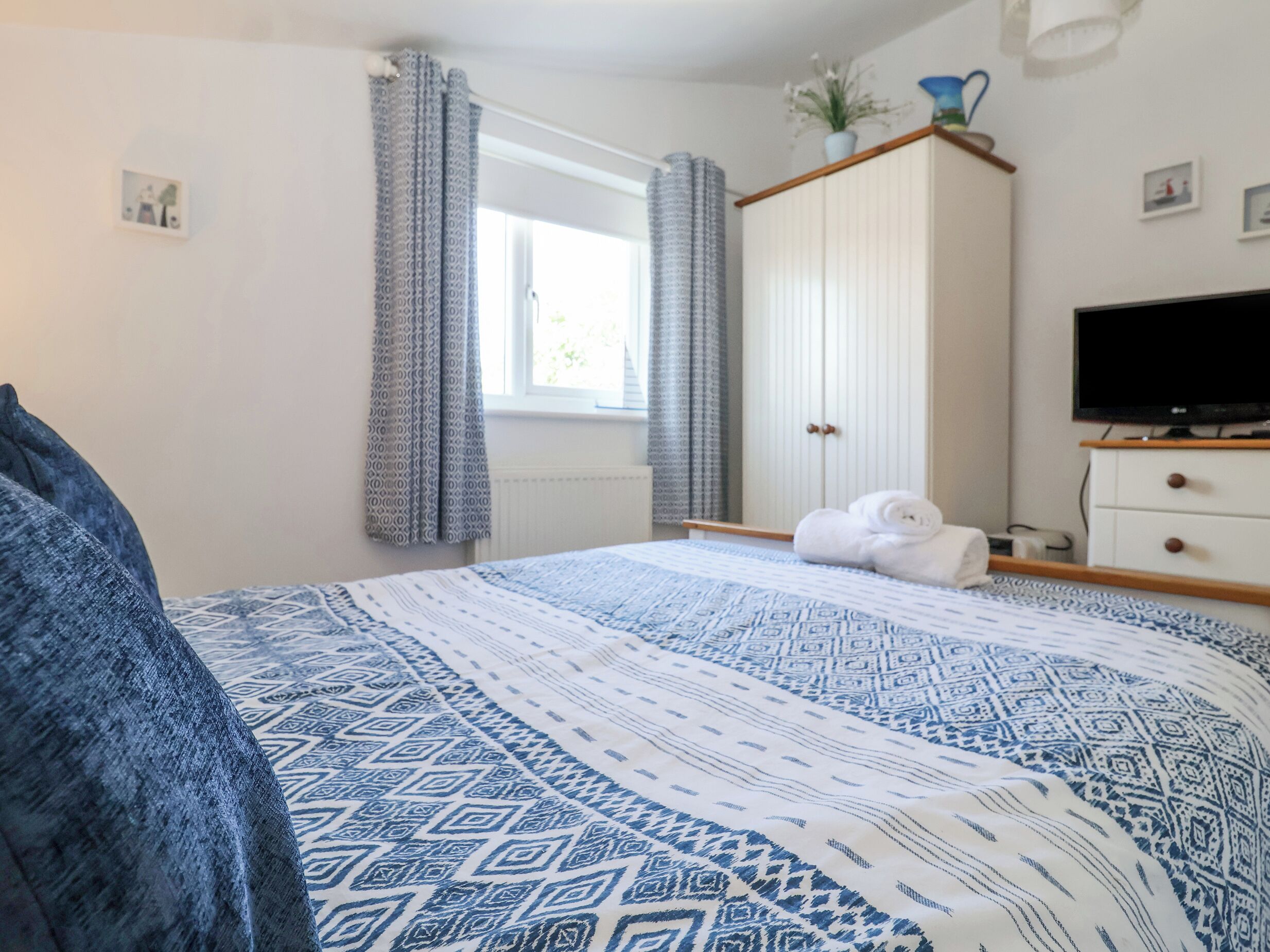 Ein Schlafzimmer mit Bett, Fernseher, Kleiderschrank und einem Fenster mit Vorhängen.