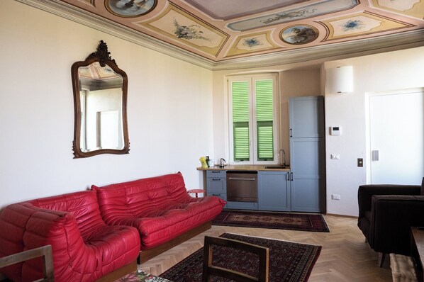 Une pièce comprenant un canapé en cuir rouge, une petite table à manger, un coin cuisine avec des placards bleus et un plafond d écoratif.