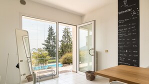 Una habitación moderna con una mesa de madera, una silla blanca y un ventanal de vidrio que da a un balcón con piscina.