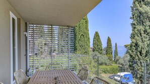 A balcony with a wooden table and wicker chairs, overlooking a parking area and a view of the sea. - Apartment Diamante with lake view and pool (Gardone Riviera)