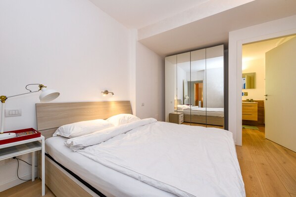 Un dormitorio moderno con una cama bien hecha, una mesita de noche con lámpara y un espejo grande.