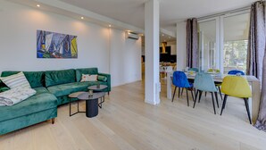 A modern living room with a green sofa, a small round table, and a dining area with colorful chairs. - Apartment Diamante with lake view and pool (Gardone Riviera)