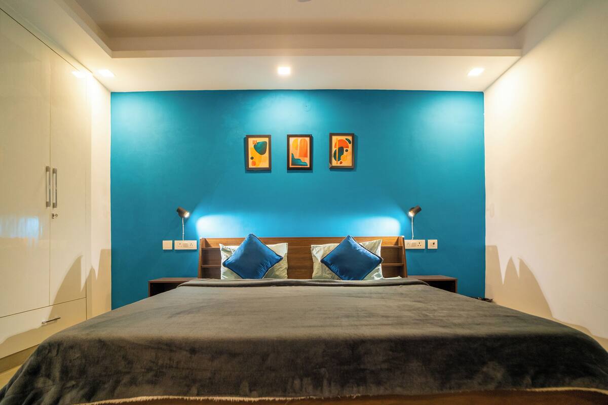 A bedroom with a large bed, blue walls, and three framed artworks above the bed.