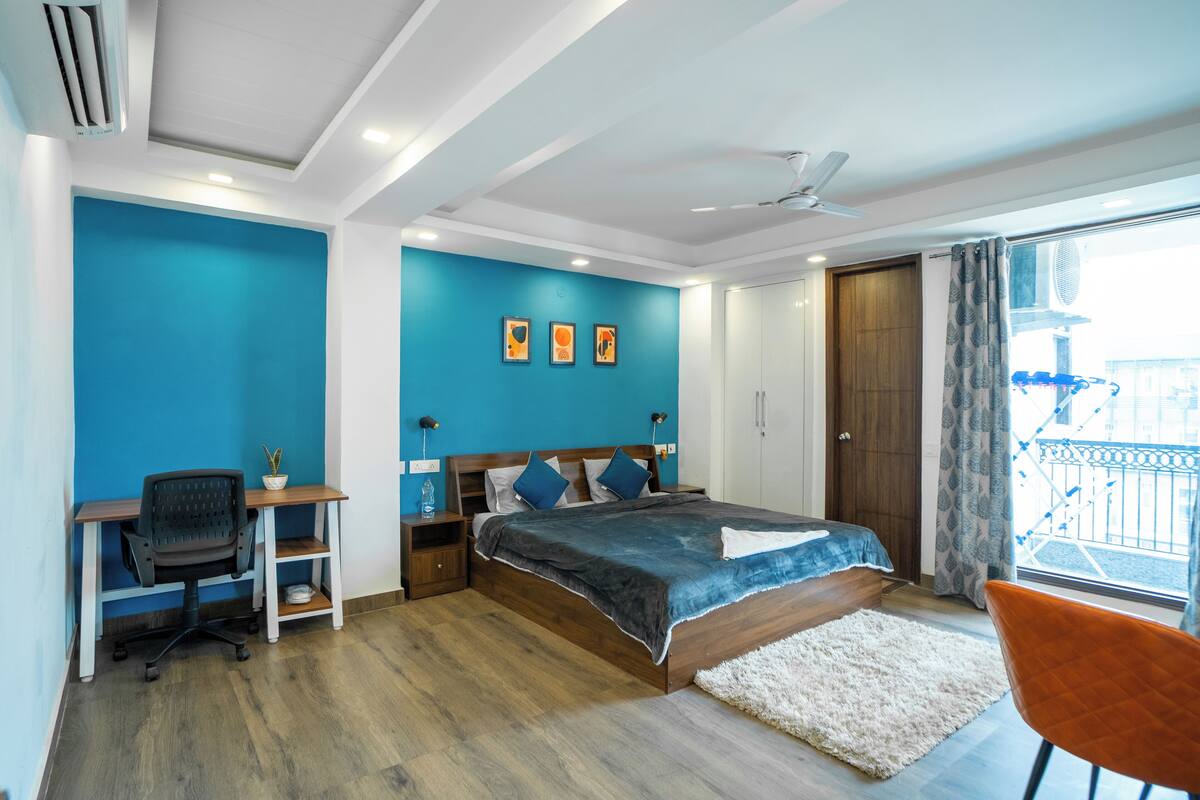 A bedroom with a bed, desk, chair, and a view of the outside.