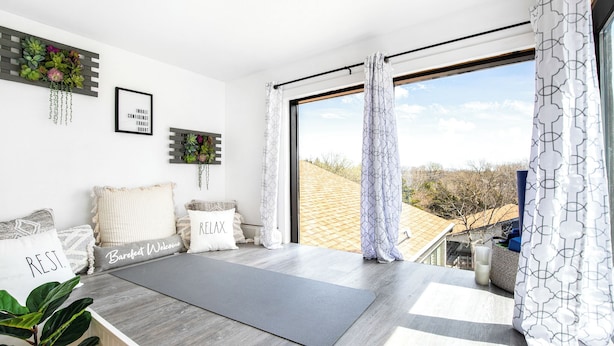 A modern room with a large window, a yoga mat, and decorative pillows with motivational phrases.
