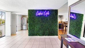 A modern interior with a neon sign reading "Lake life" on a green wall, a kitchen area with stainless steel appliances, and a dining space with wooden chairs.