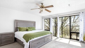 A bedroom with a bed, nightstands, a ceiling fan, and large windows.