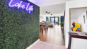 A modern living room with a neon sign reading "Lake Life," a dining area with wooden furniture, and a hallway leading to another room.