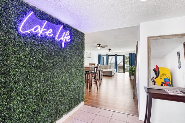Un interior moderno con un letrero de neón que dice "Lake Life", un comedor con muebles de madera y un pasillo luminoso que conduce a una sala de estar.