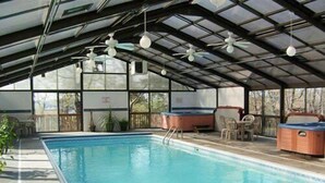 An indoor swimming pool with a covered roof, ceiling fans, and seating areas.