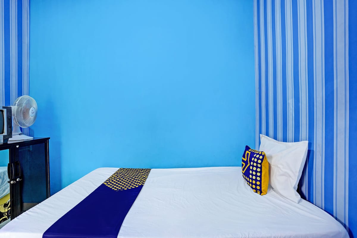 A hotel room with a bed, a nightstand, a fan, and blue-striped curtains.