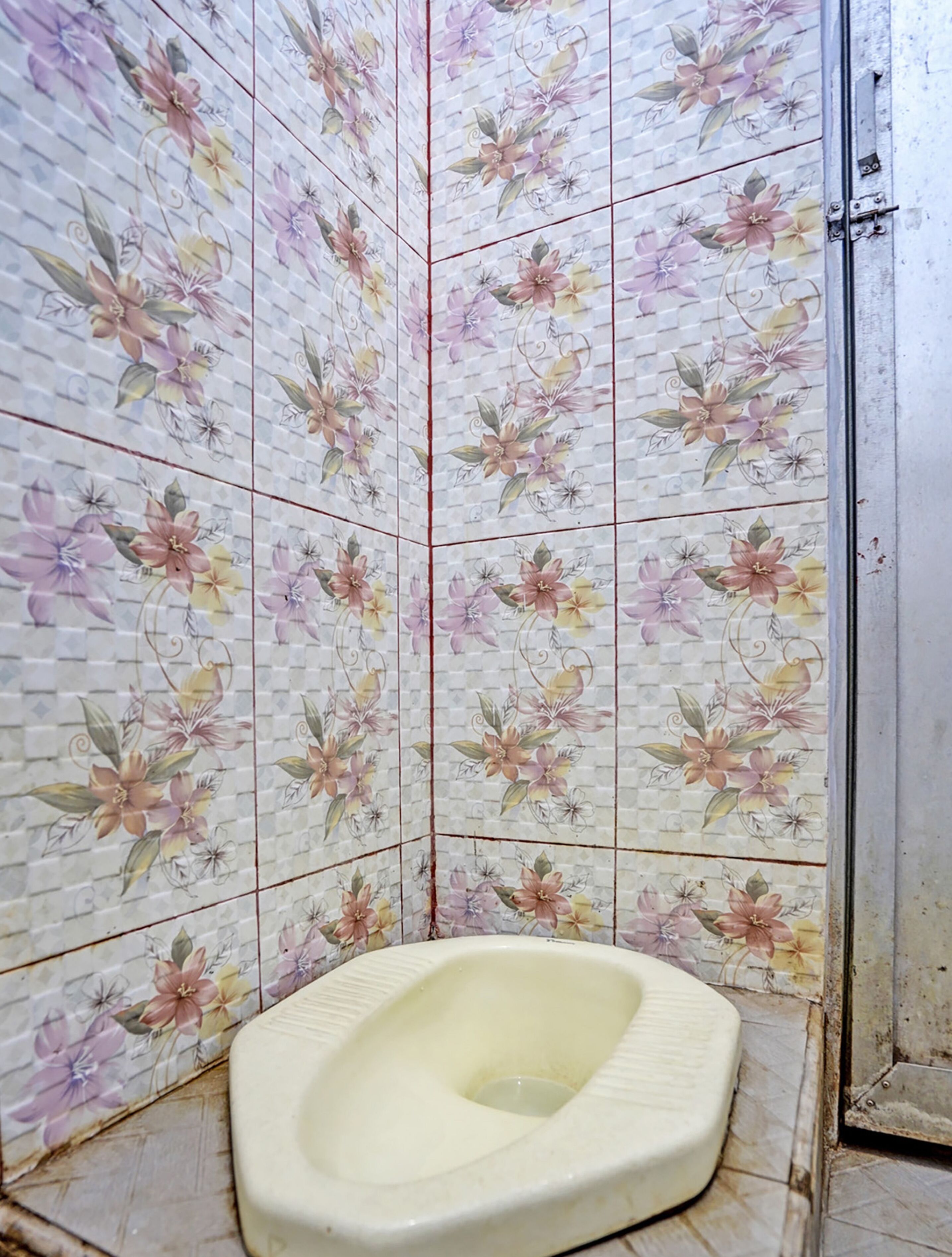 A bathroom with a toilet, tiled walls with floral patterns, and a metal door.