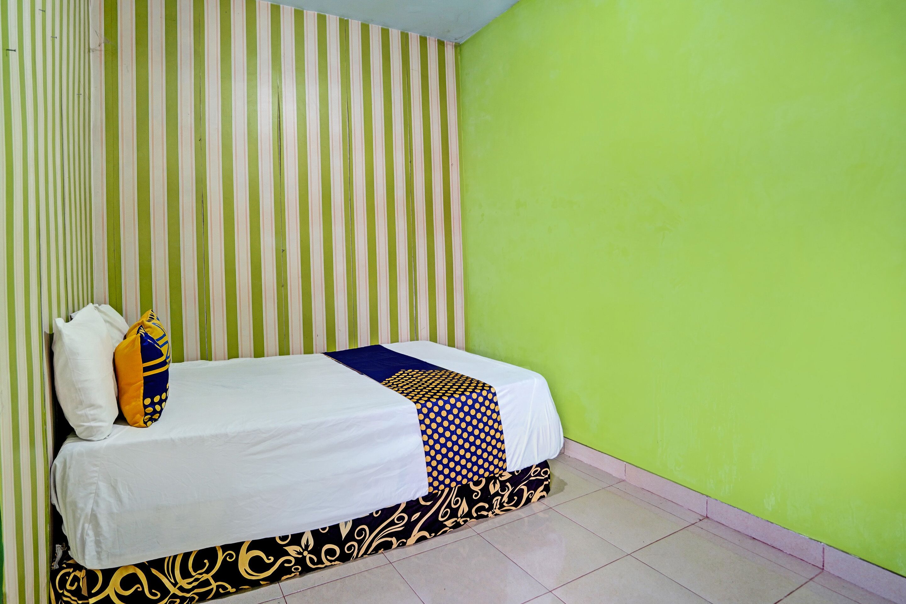 A single bed with a white and patterned bedspread, two pillows, and a striped wall behind it.