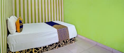 Un lit simple avec une couvre-lit blanche à motifs, deux oreillers et un mur à rayures derrière.