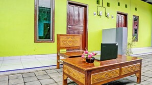 A wooden desk with a laptop and a vase of flowers, placed outside a building with green walls and a tiled floor. - Hotel O Gang Songo Syariah HomestayNearWisata Osing (Rogojampi)