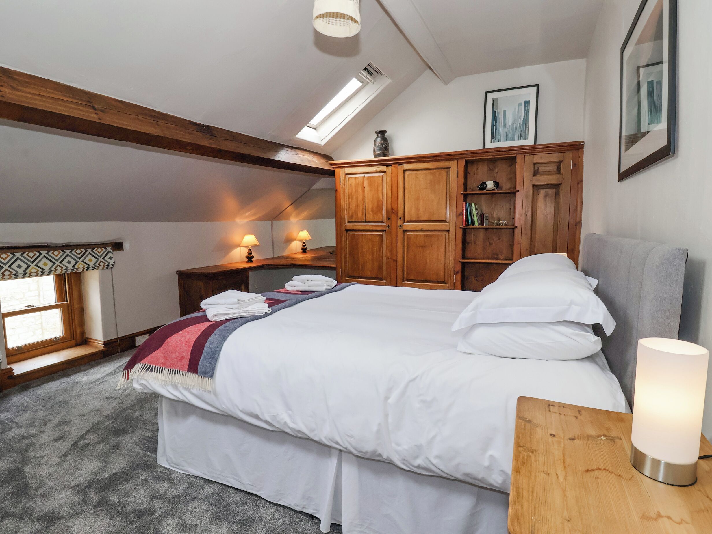 A bedroom with a bed, wooden wardrobe, bedside lamps, a window with a view, and a skylight.