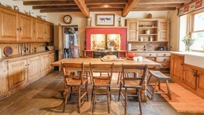 Une cuisine rustique avec des meubles en bois, un sol en pierre et une grande table en bois entourée de chaises.