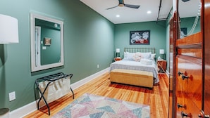 Un dormitorio con cama, mesita de noche, cómoda, espejo, ventilador de techo y alfombra estampada.