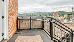 Un balcón con vista a un paisaje urbano, un muro de ladrillo y una reja metálica.