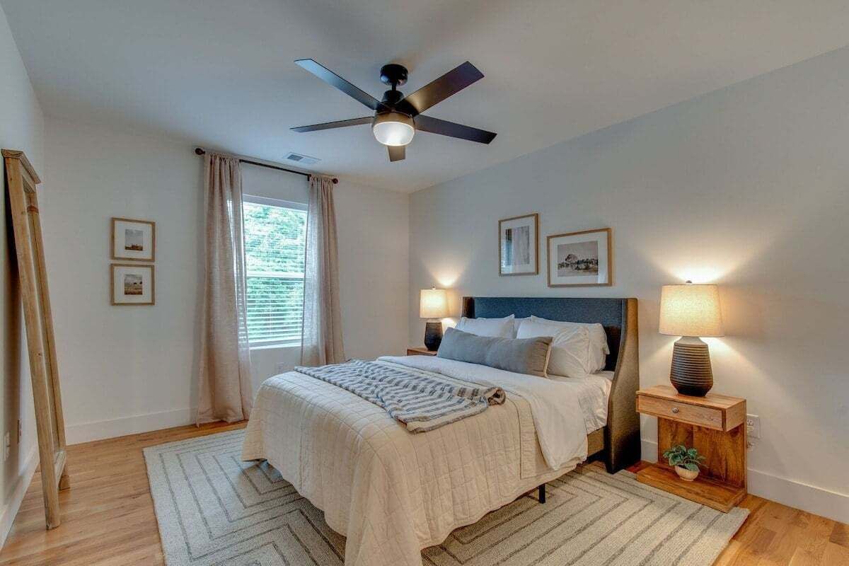 Un dormitorio con cama, lámparas de noche, ventilador de techo y ventana con cortinas.
