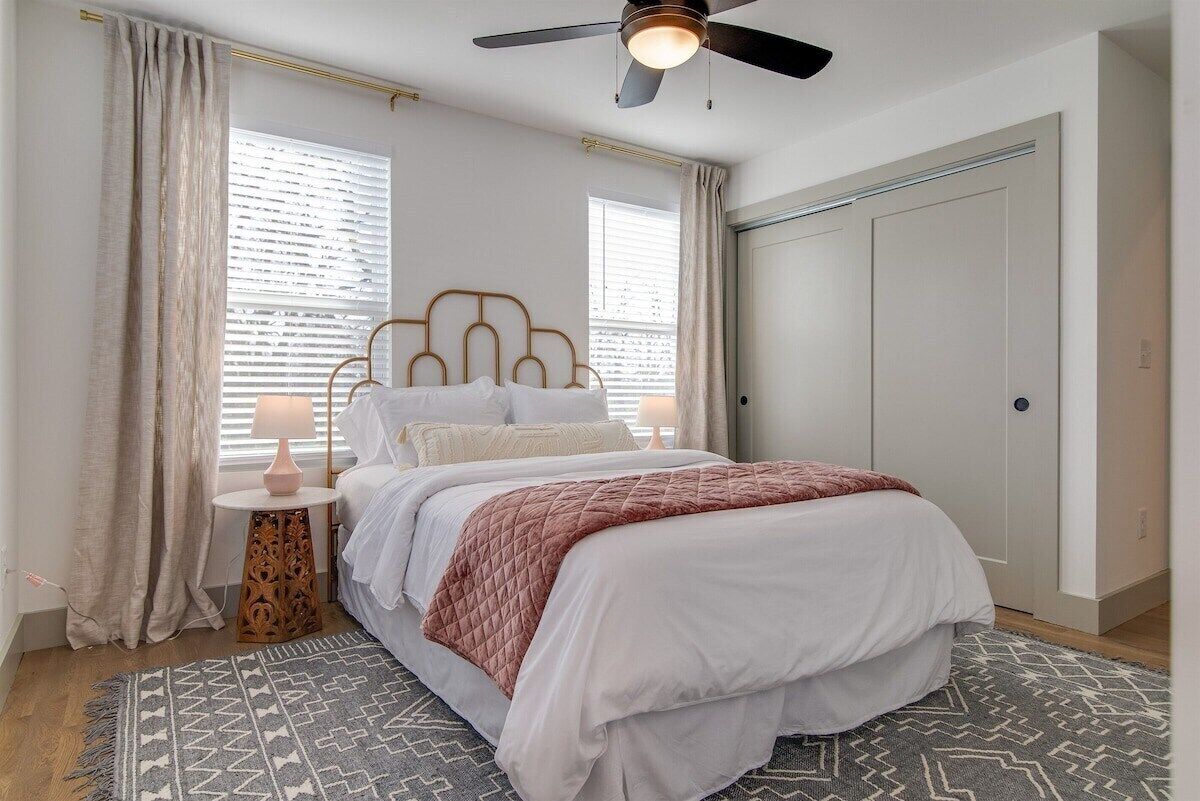 A bedroom with a bed, a ceiling fan, a bedside table with a lamp, and a patterned rug.