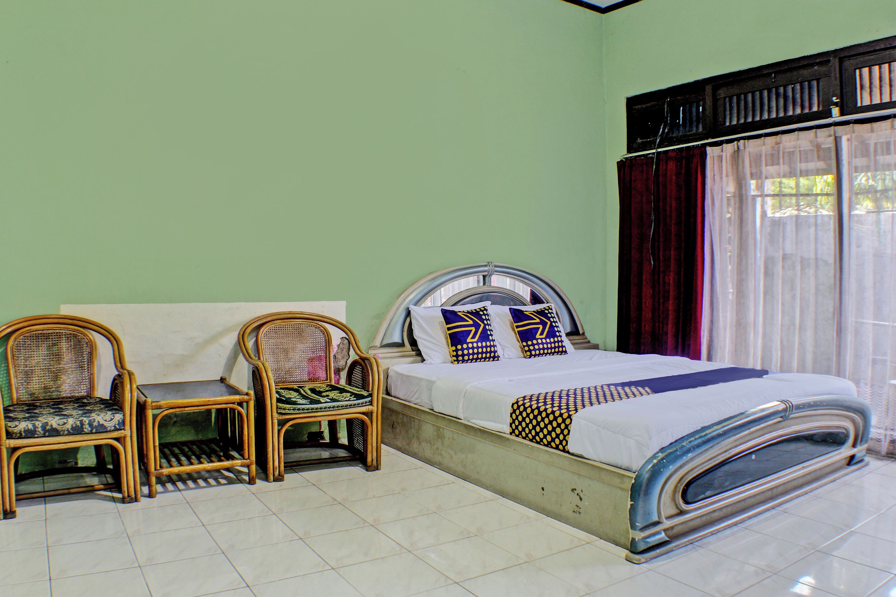 A room with a bed, two chairs, and a window with curtains.