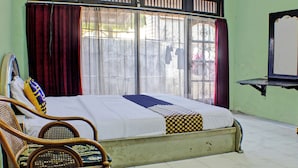 A room with a bed, a chair, a window with curtains, and a mirror on the wall. - Hotel O Badar Guest House Syariah (Bandar Lampung)