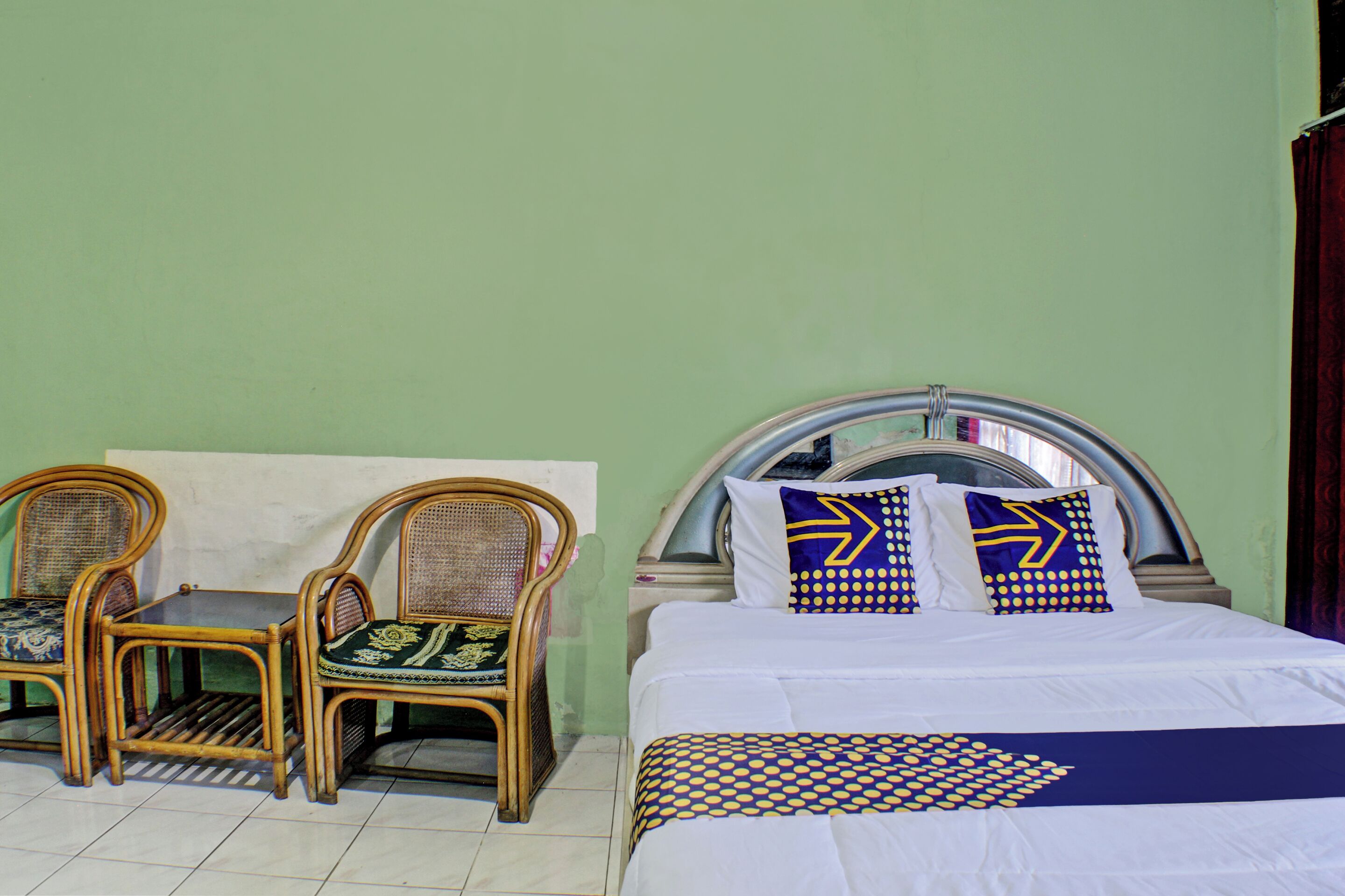 Ein Zimmer mit einem Bett, zwei Korbstühlen und einem kleinen Tisch.