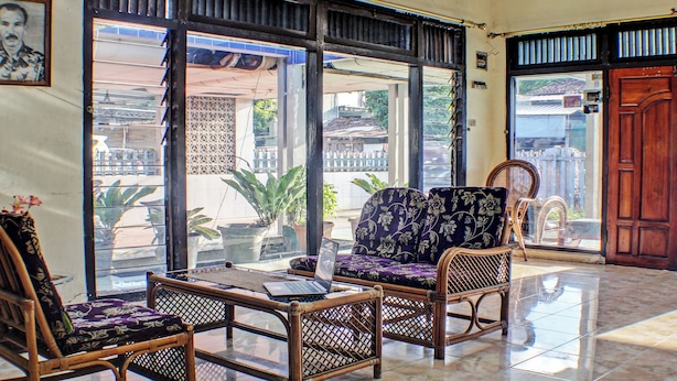 A room with wicker furniture, a laptop on a table, and a view through large glass doors. - Hotel O Badar Guest House Syariah (Bandar Lampung)