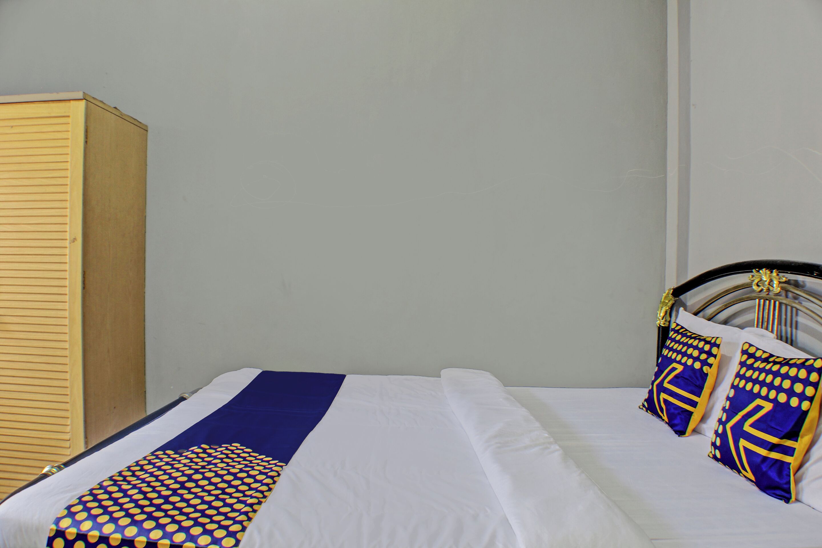 A bed with white bedding, a blue and yellow patterned bedspread, and two decorative pillows with geometric designs.
