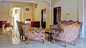 A spacious living room with a high ceiling, a wooden coffee table, and ornate armchairs. - Hotel O Badar Guest House Syariah (Bandar Lampung)