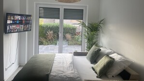 Ein Schlafzimmer mit einem Bett, einem an der Wand montierten Fernseher, einem großen Fenster und einer Pflanze.