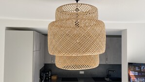Eine moderne Küche mit grauen Schränken, einer schwarzen Arbeitsplatte und einer gewebten Rattan-Pendelleuchte.