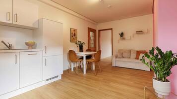 A modern kitchen with white cabinets, a dining table with two chairs, and a living area with a sofa and a potted plant.