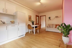 A modern kitchen with white cabinets, a dining table with two chairs, and a living area with a sofa and a potted plant. - homie stay badgasse - am Main mit Dachterrasse (Ochsenfurt)