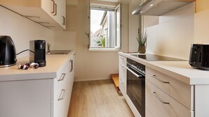 Et lille køkken med hvide skabe, en indbygget ovn og et vindue, der giver naturligt lys.