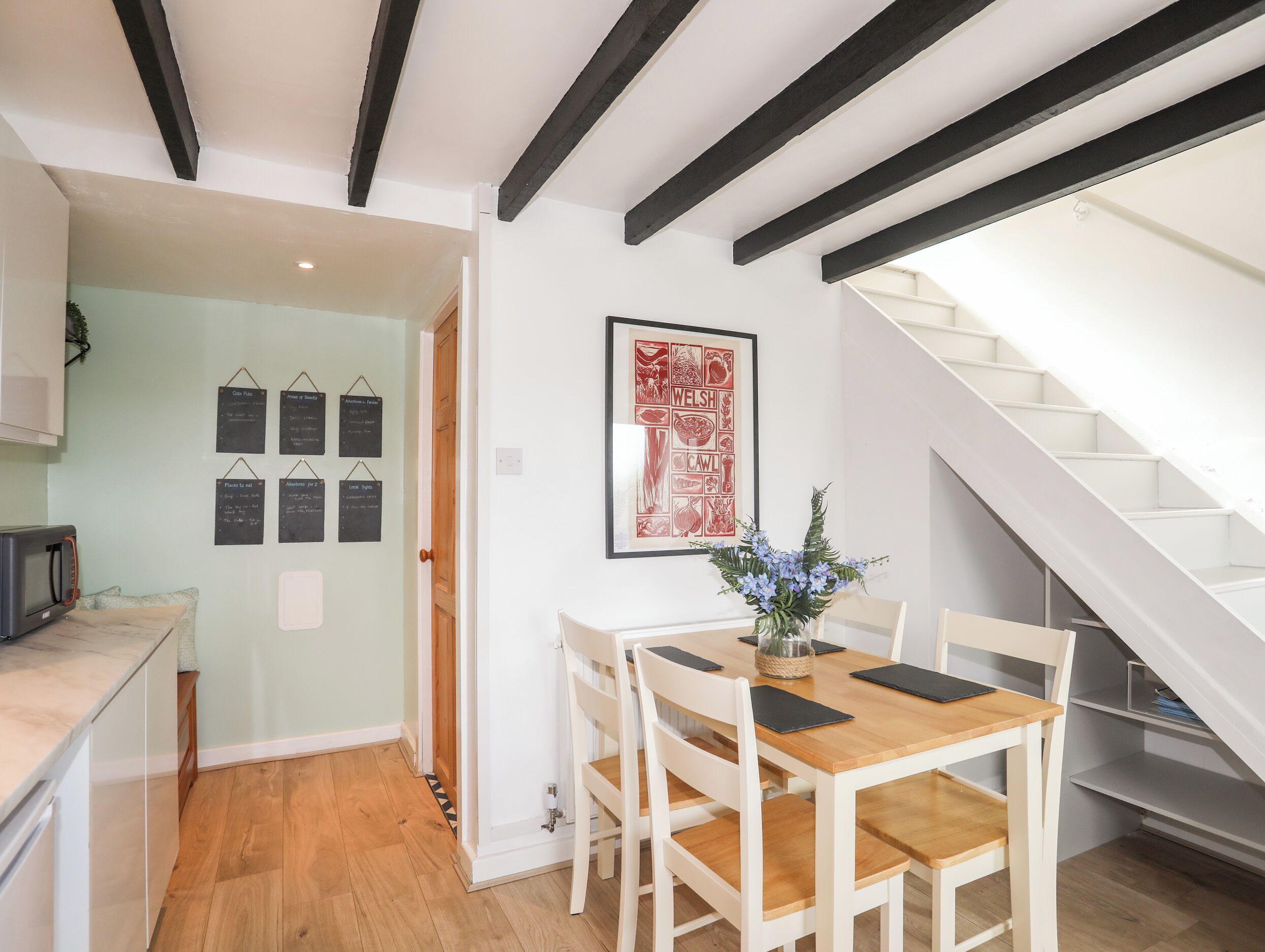 Ein Essbereich mit einem Holztisch und Stühlen, einer gerahmten Speisekarte an der Wand und einer Treppe rechts.