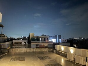 A rooftop terrace with tiled flooring, a metal railing, and a view of the city skyline at dusk. - FlxHo Duo-Golf Course Road (Gurugram)