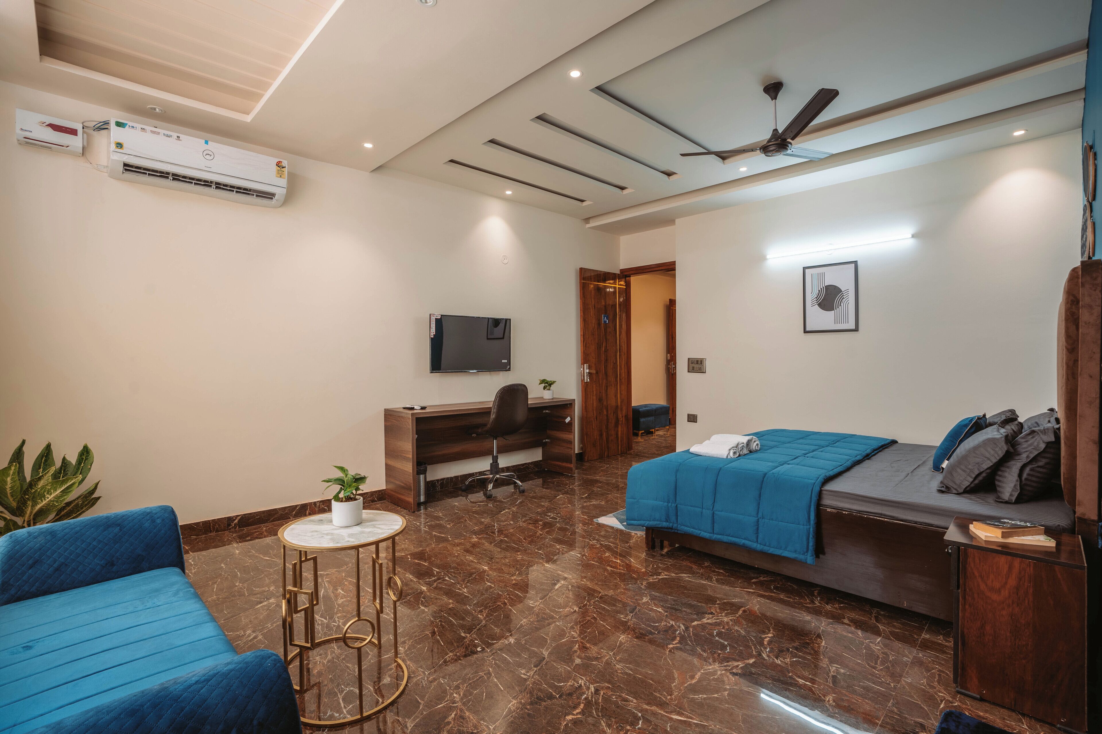 Ein modernes Hotelzimmer mit Bett, Schreibtisch, Stuhl, Fernseher und Deckenventilator.