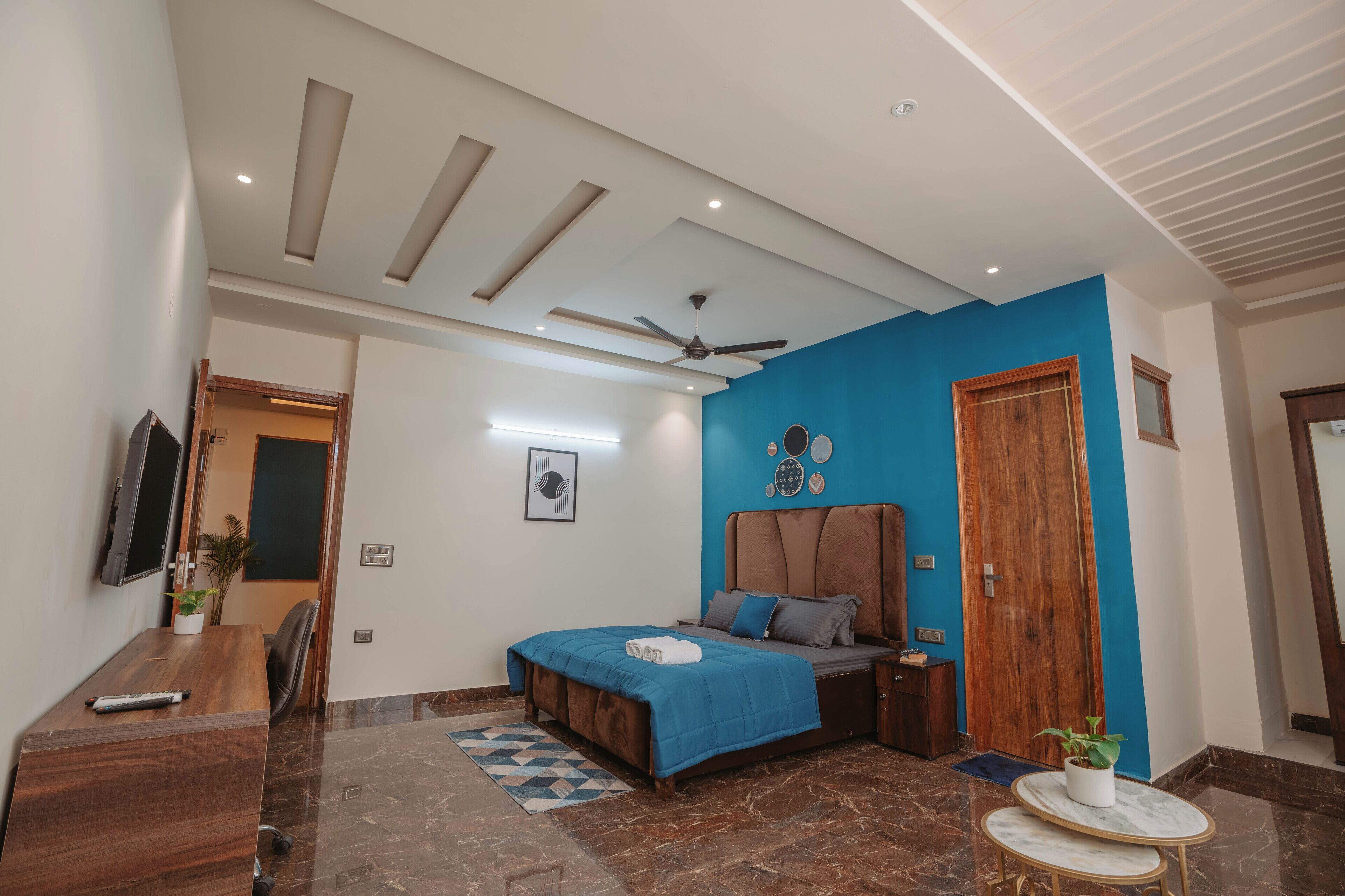 A bedroom with a bed, a desk, a ceiling fan, and a blue accent wall.